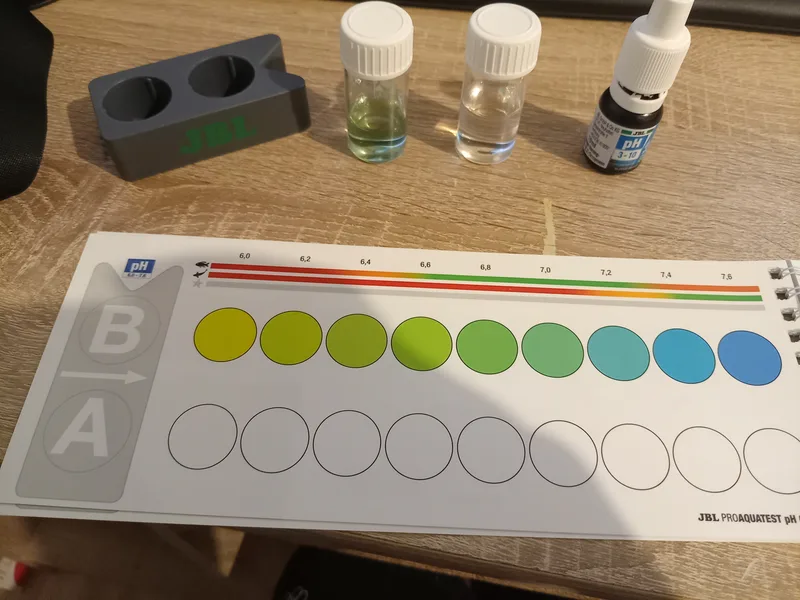 Test de pH JBL ProAquaTest : flacon d'eau du bac avec réactif comparé à la carte de couleurs de 6,0 à 7,6